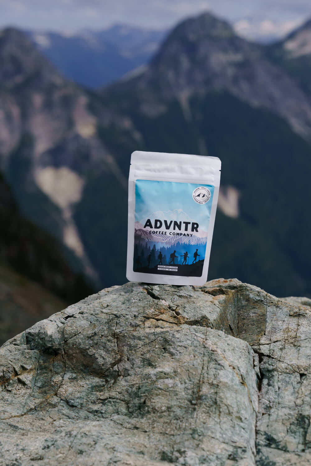 3 ounce coffee bag from adventure coffee roasters sitting on a rock with a mountain background