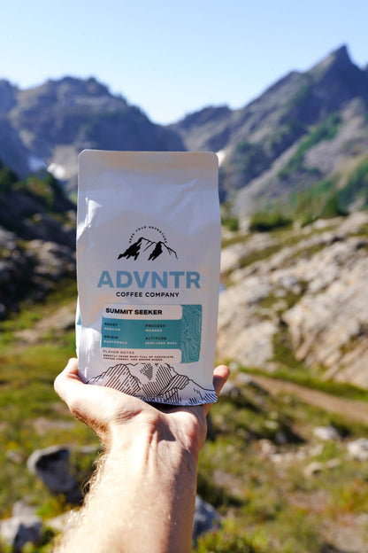 hand holding summit seeker coffee bag from advntr coffee co with mountains in the background