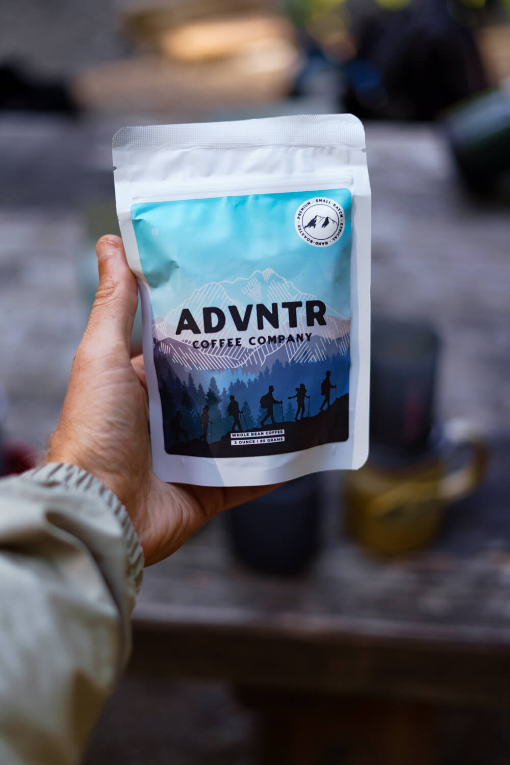hand holding advntr coffee bag with blurry table in the background