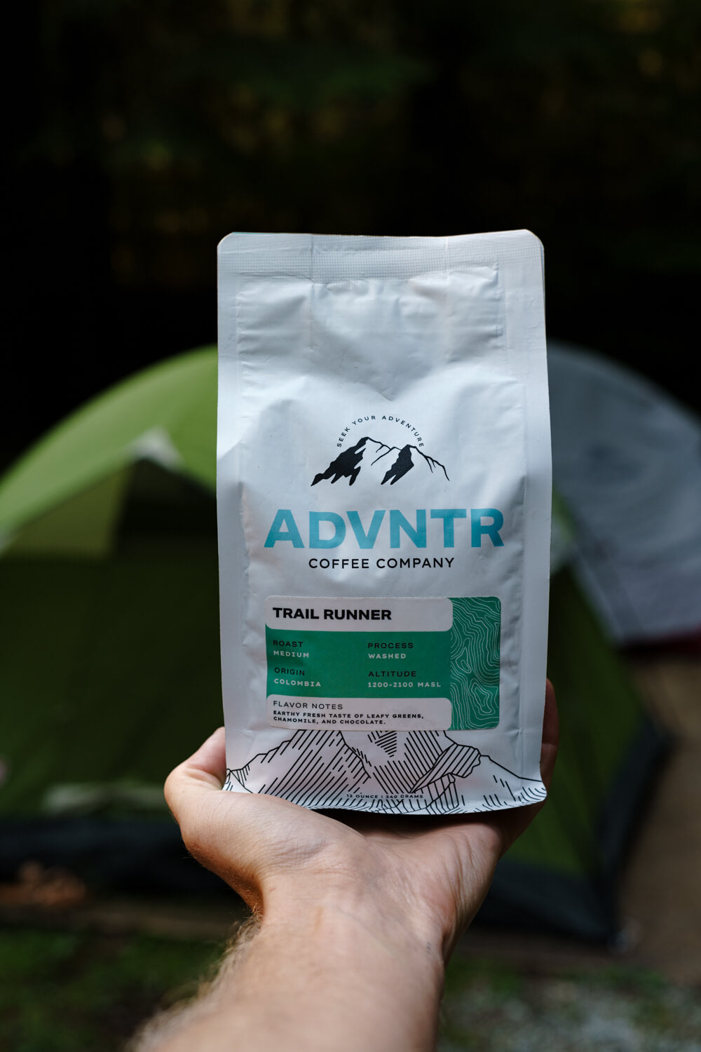 hand holding adventure coffee bag with tents in the background