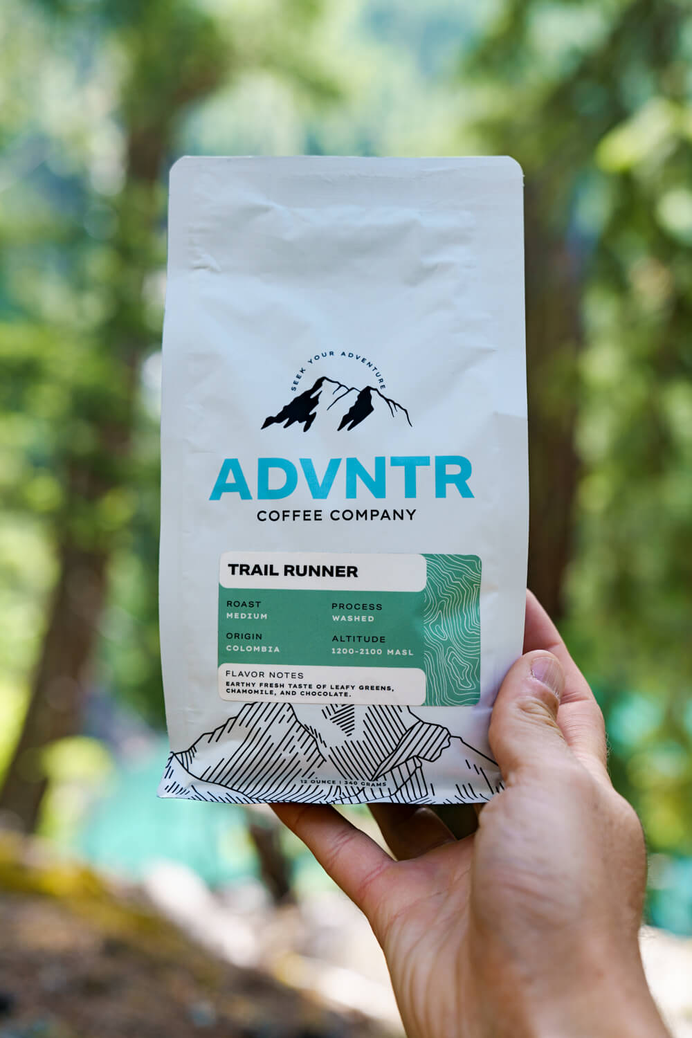 hand holding trail runner coffee bag by advntr coffee company with trees in background